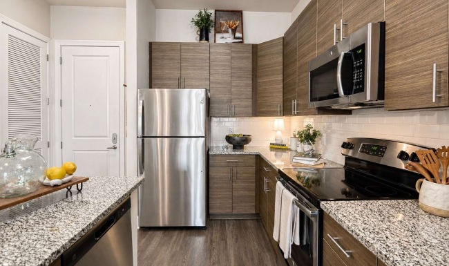 Upscale apartment kitchen with polished stone countertops, warm wood cabinetry, stainless steel appliances, and refined modern lighting.