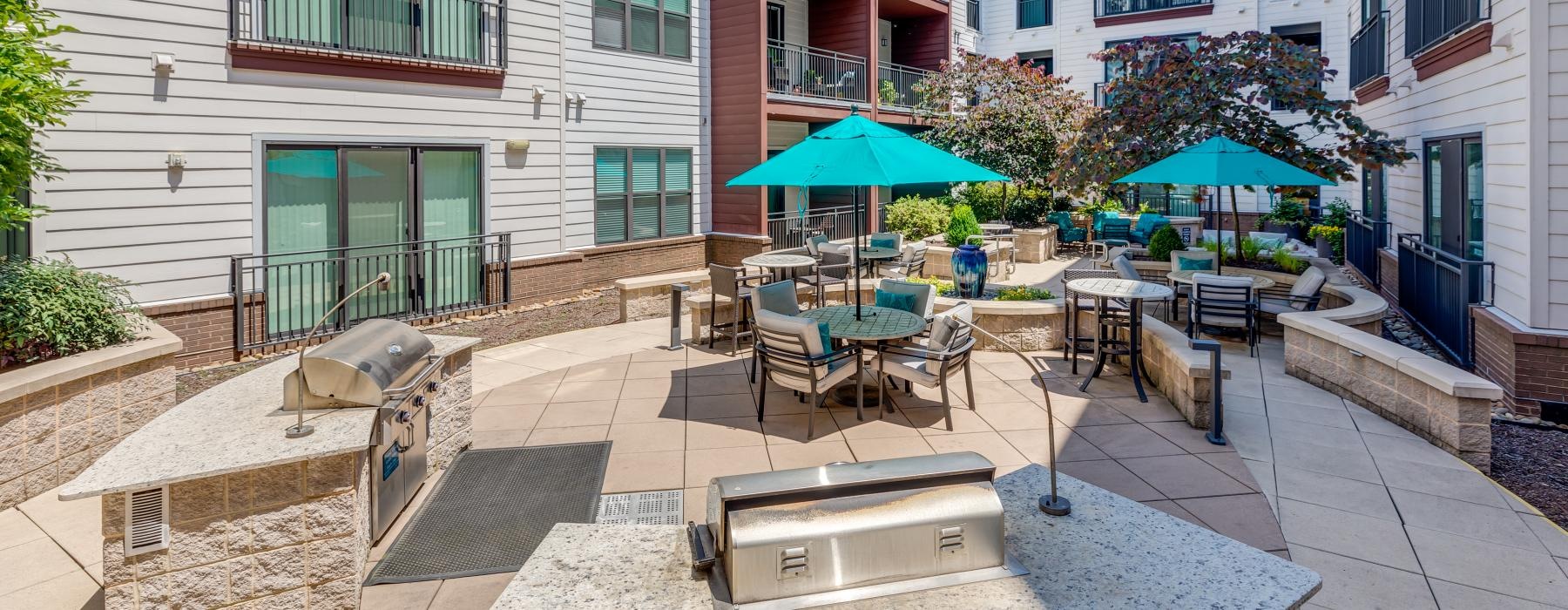 a patio with chairs and tables and grill and umbrellas in front of a building